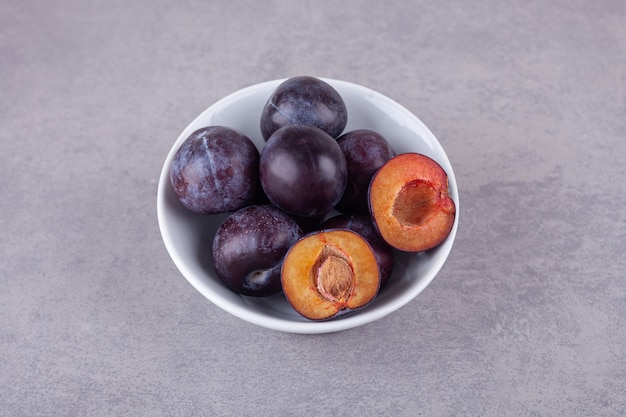 Bunch of fresh purple plums placed on stone surface.