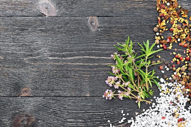 Bunch of fresh thyme with green leaves and pink flowers with salt pepper fenugreek seeds on a black wooden board background