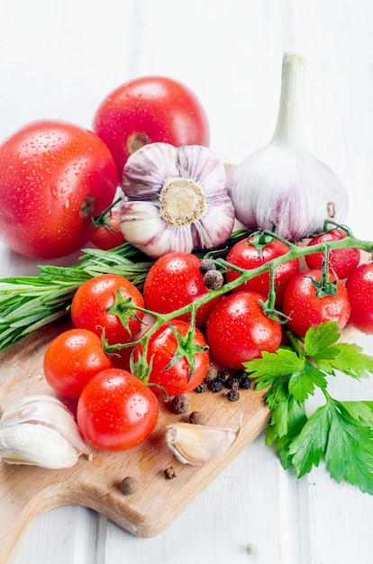 Bunch of juicy organic red cherry tomatoes with green  rosemary,  garlic and spices on white old table. Ingredients for cooking. Clean eating concept. Vegetarian diet. space for text