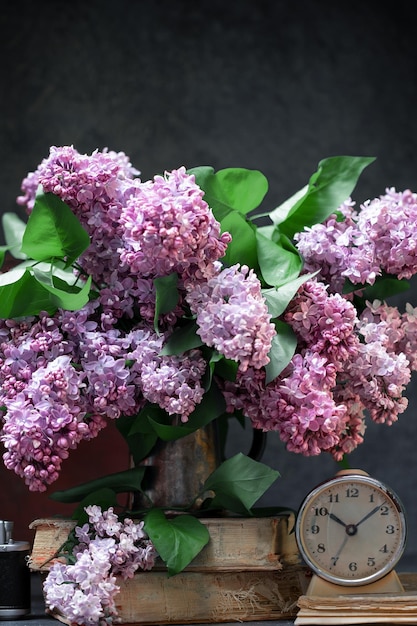 Bunch of lilac flowers with old books and vintage alarm clock