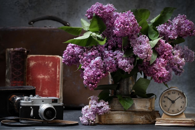 Bunch of lilac flowers with a vintage suitcase old books and alarm clock