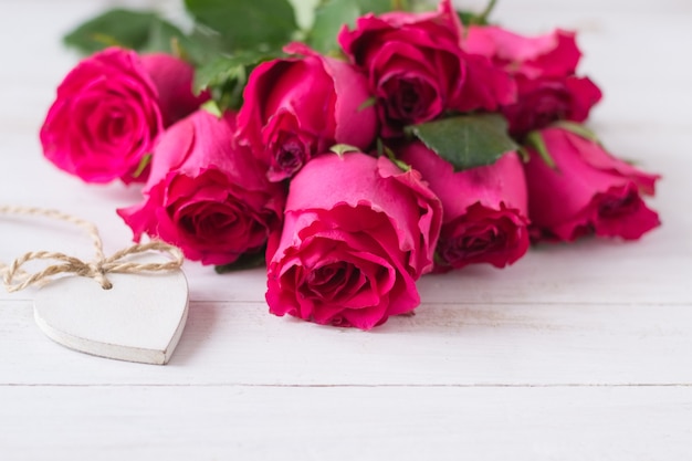 Bunch of pink roses and white wooden heart on wooden table