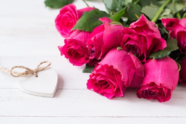 Bunch of pink roses and white wooden heart on wooden table