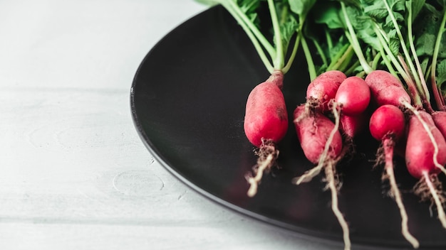 Bunch of radishes in a black plate on a white wooden background