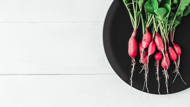 Bunch of radishes in a black plate on a white wooden background