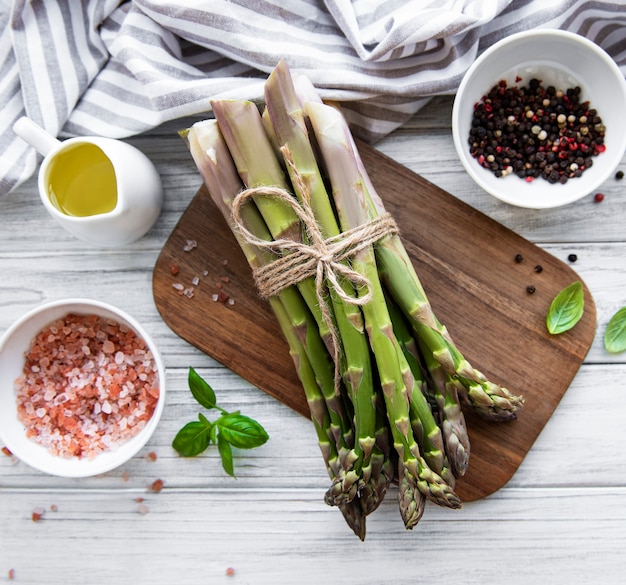 Bunch of raw asparagus stems with different spices and ingredients on wooden table. Top view, flat lay.