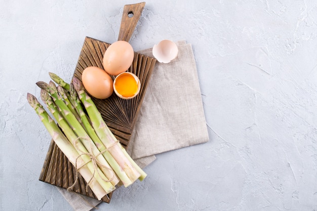 Bunch of raw fresh asparagus with eggs on a gray concrete background