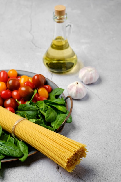 A bunch of raw spaghetti with spinach, tomato, garlic and olive oil