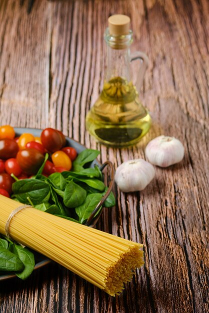 A bunch of raw spaghetti with spinach, tomato, garlic and olive oil