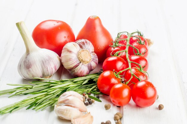 Bunch of red cherry tomatoes with green rosemary garlic and spices on white old table