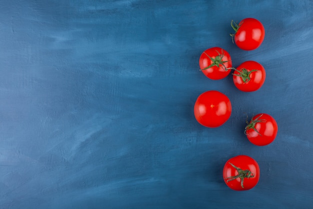 Bunch of red fresh tomatoes placed on blue surface.