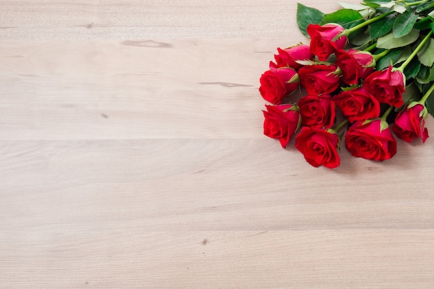 A bunch of red roses on wooden background with space for text