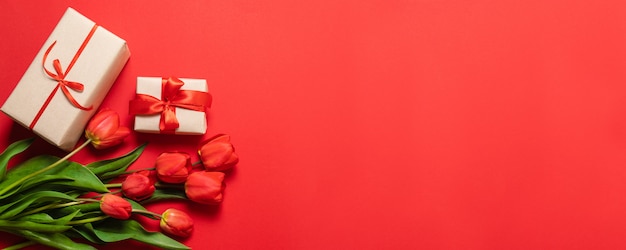 Bunch of red tulips and gift boxes with red ribbons on a red background. 