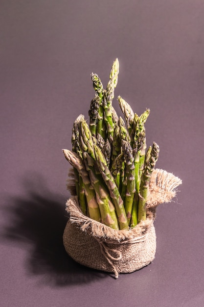 A bunch of ripe asparagus in a burlap napkin. Fresh ingredient for healthy food, black stone cooking background, copy space