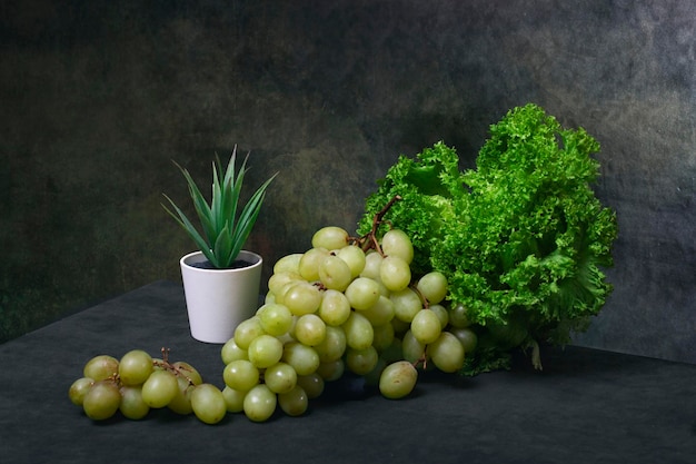 A bunch of ripe grapes with green lettuce leaves and cactus in a pot