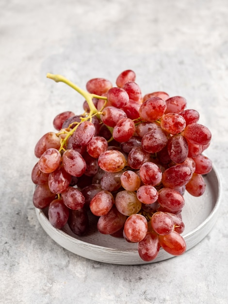 A bunch of ripe red grapes with the drops of water on it on gray ceramic plate 