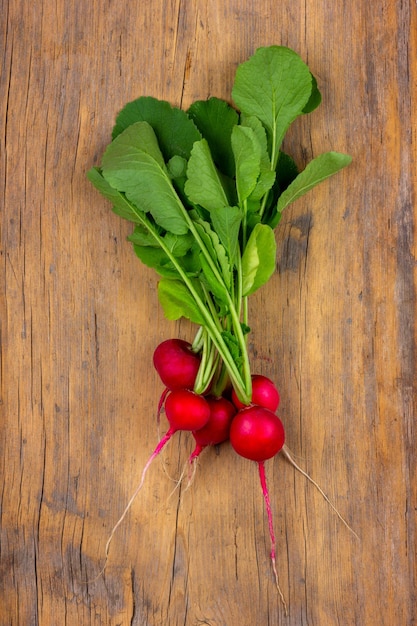 Bunch ripe red radish with green leaves on a wooden background top view