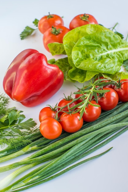 A bunch of tomatoes and green onions are on a white surface.