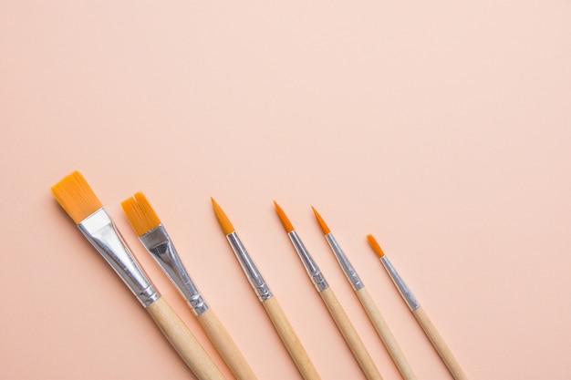 Bunch of Various Kinds of Paint Brushes on Light Pink Peachy Background.