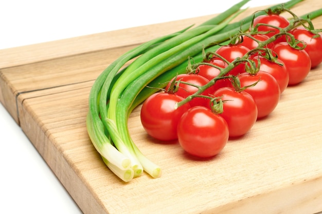 Bunches of fresh red cherry tomatoes and young green onion on cutting board isolated on white background Ripe tomatoes on green stems Bunch of fresh onion Fresh organic vitamin vegetables