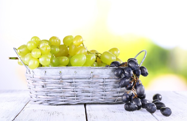 Bunches of ripe grape in wicker basket on wooden table on natural background