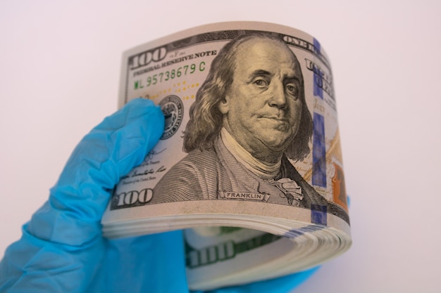 Bundle of one hundred dollar bills rolled up in hand in medical glove on white background