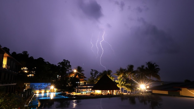 Bungalows with palm trees of a tropical island against the light at dark sky with lightning