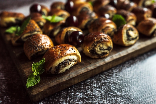 Buns with poppy seeds with cherries mint leaves on a brown wooden board on a gray background 5