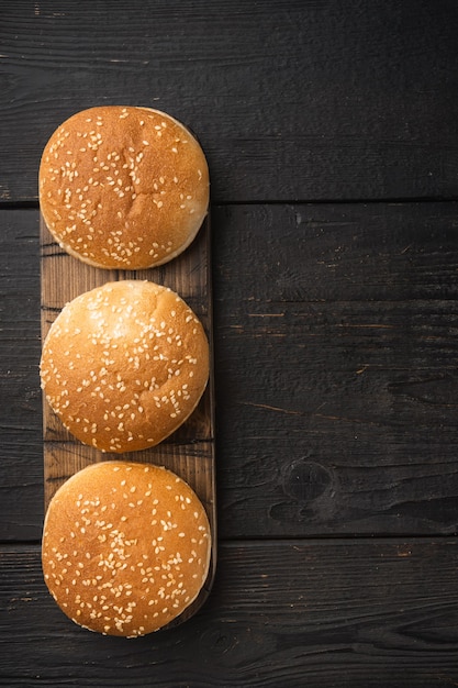 Burger buns, homemade sesame buns patty Brioche for sandwich set, on wooden serving board, on black wooden table, top view flat lay