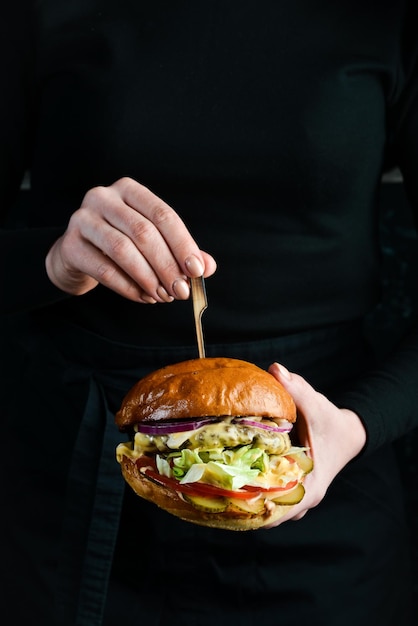 Burger in the hands of the chef Fast food concept On a dark background