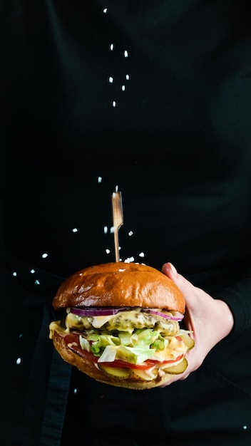 Burger in the hands of the chef Fast food concept On a dark background