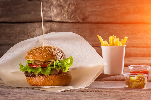 Burger on paper and fries Table with beefburger and fries Sliced pickles and fast food Highcalorie lunch at restaurant