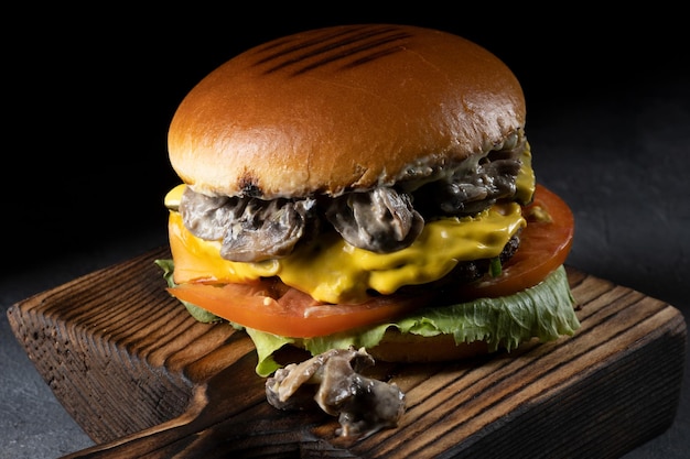 Burger with bacon meat tomato and lettuce on wooden board and black background Close up