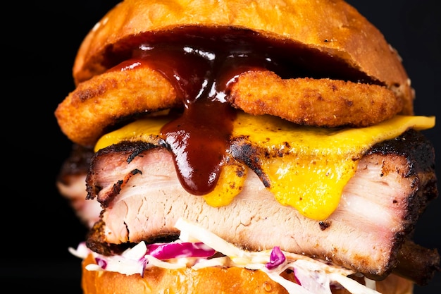 Burger with bbq pork rib onion rings cheese cabbage and lettuce on a black Closeup macro view