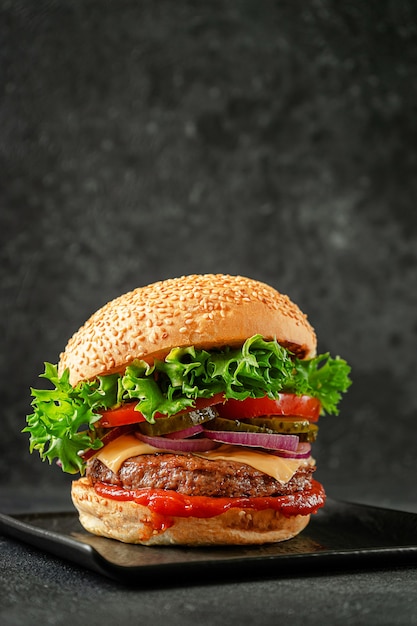 Burger with beef, cheddar cheese, onion,tomato,lettuce and pickled cucumber on slate plate. American street food