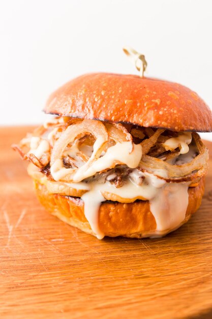 Burger with beef cutlet under tender cream cheese with champignons and onion chips on a wooden plate on a white background Vertical photo