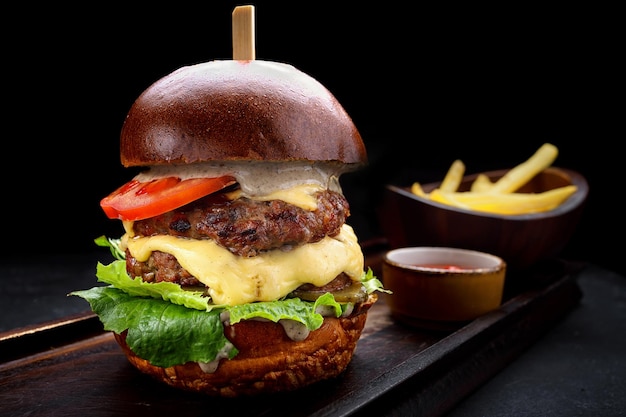 Burger with double meat patty cheese and vegetables French fries sauce Black background