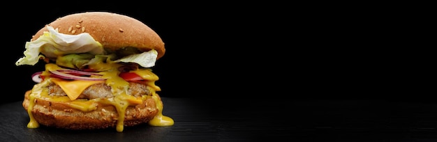 Burger with meat tomato lettuce cheese and onion on a black background Fastfood with place for your text selective focus