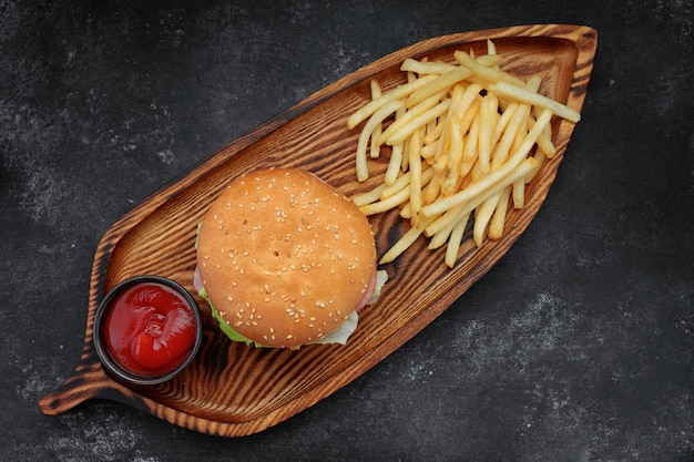 Burger with meat tomatoes and cheese french fries and sauce on a black background top view