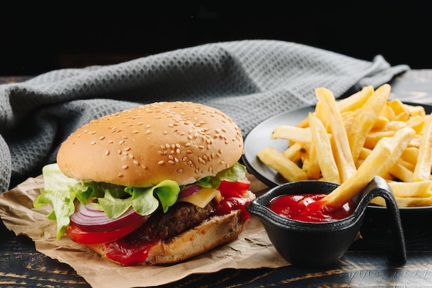 Burger with sauce and French fries beef burger with cheese bacon leafs onion and french fries on wood table