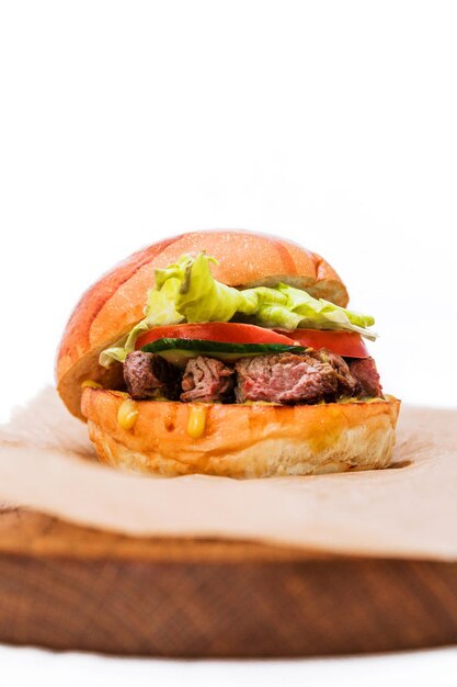 Burger with tender beef roast beef tomato cucumber lettuce and cheese sauce on a wooden plate on a white background