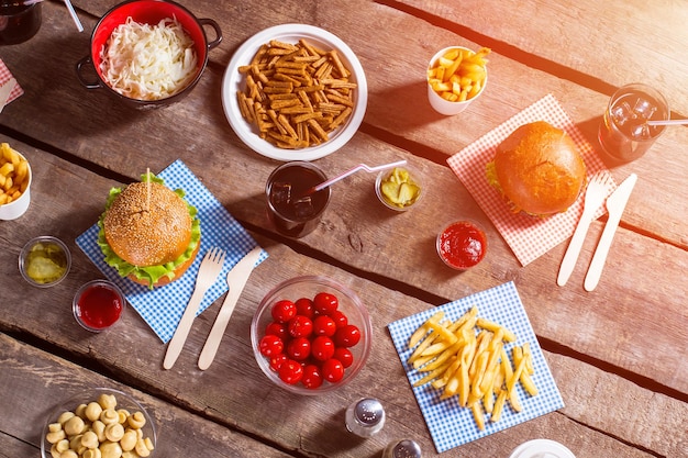 Burgers on sticks and tomatoes Food and spices on table Pile of fries and crackers Food prepared for a picnic