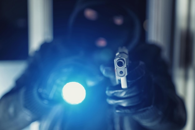 Burglar or a thief holding a gun with flashlight in a house