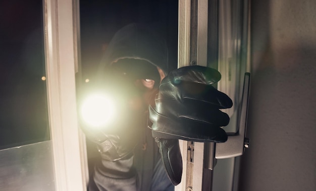 Burglar using flashlight to break into a house at night