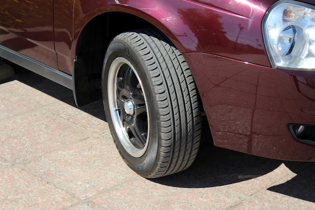 Burgundy car. Car wheels under the bright sun. New shiny car and wheel in direct sunlight and in the open air standing on the asphalt.