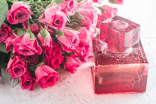 Photo burgundy square perfume bottle on glossy surface with delicate pink roses and water drops. eau de toilette.