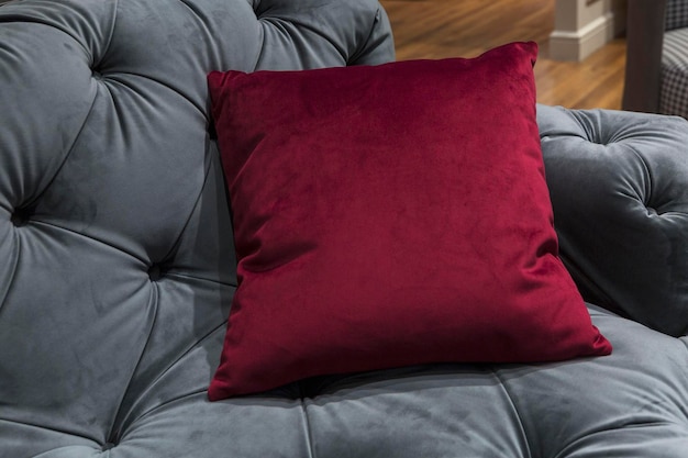 Burgundy throw pillow on a gray quilted modern sofa Fashionable interior design and decor Closeup