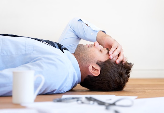 Burned out businessman overworked A businessman lying on the floor with hand rested on his head and paperwork lying on the floor in front of him