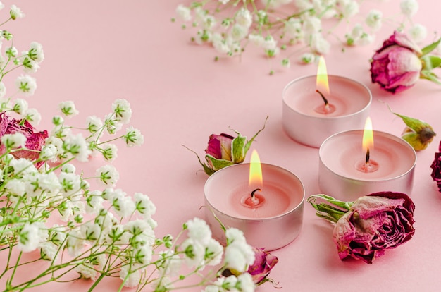 Burning aroma candles with flowers and dried roses on pink. SPA and aromatherapy concept.