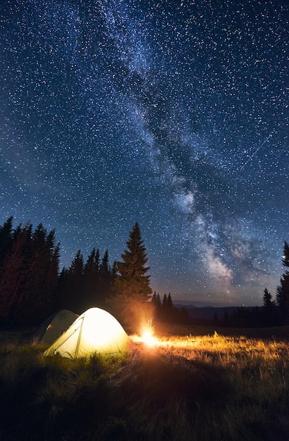 Burning bonfire and tents under bright starry sky on which the Milky Way is clearly visible Magical sky